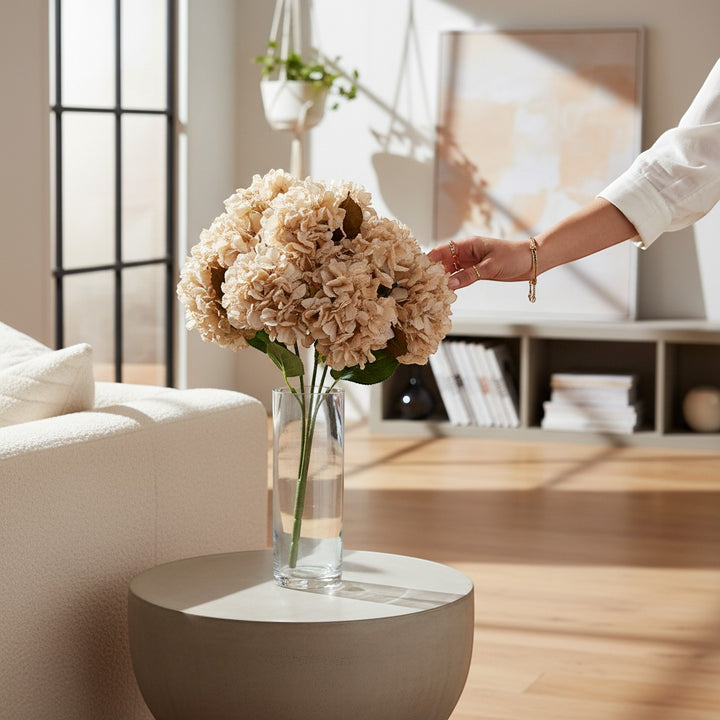 Chic Collective 24" beige artificial hydrangea spray in a clear glass vase on a round table.
