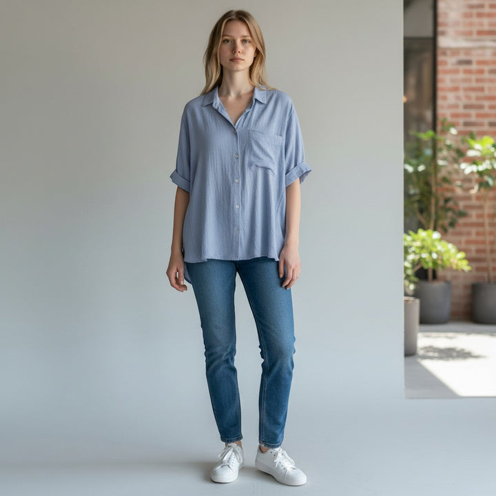 Chic Collective light blue textured short-sleeve button-up top with a chest pocket, cuffed sleeves, and a relaxed fit, paired with blue jeans.