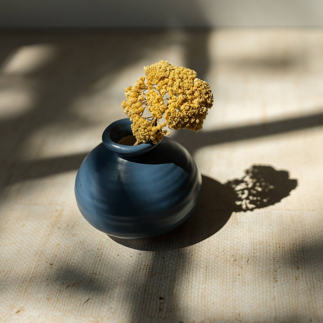 Chic Collective Mattie blue matte stoneware bud vase with ribbed texture, holding a single dried yellow bloom.