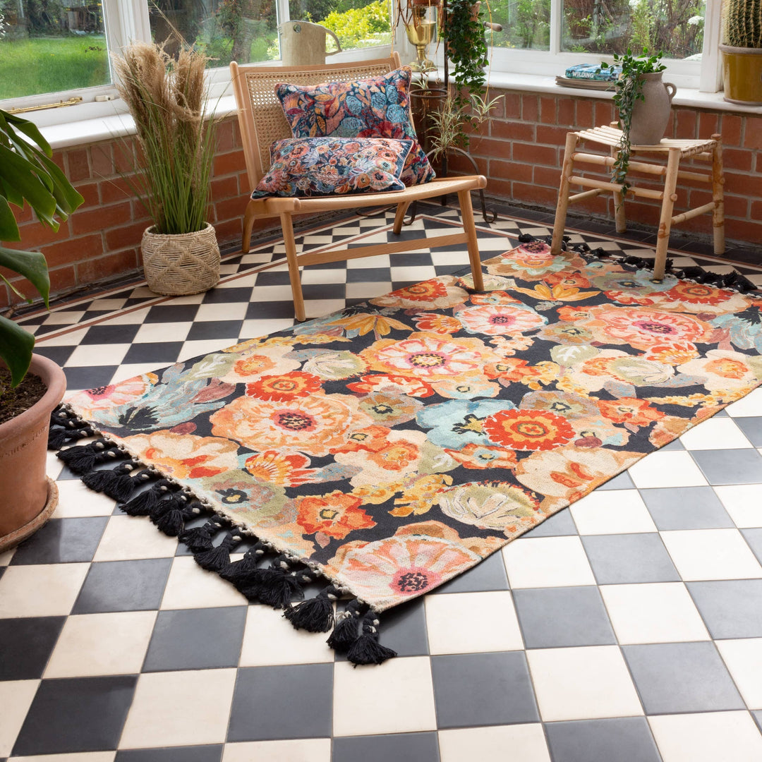 Chic Collective Florage rug with a bold floral print in peach, orange, and blue on a dark background, featuring black tassels.