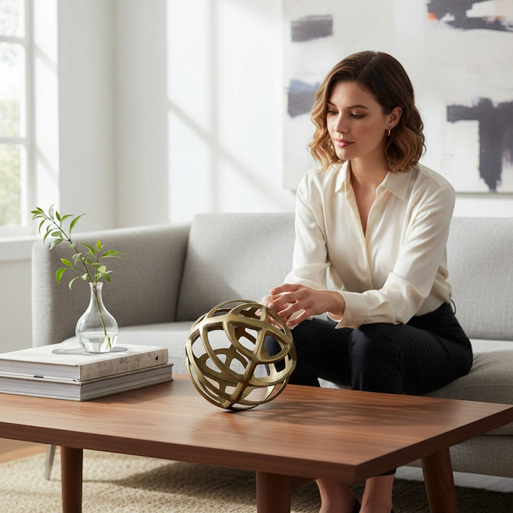 Chic Collective gold metal geometric sphere decor on a coffee table, featuring an open, intersecting rod design.