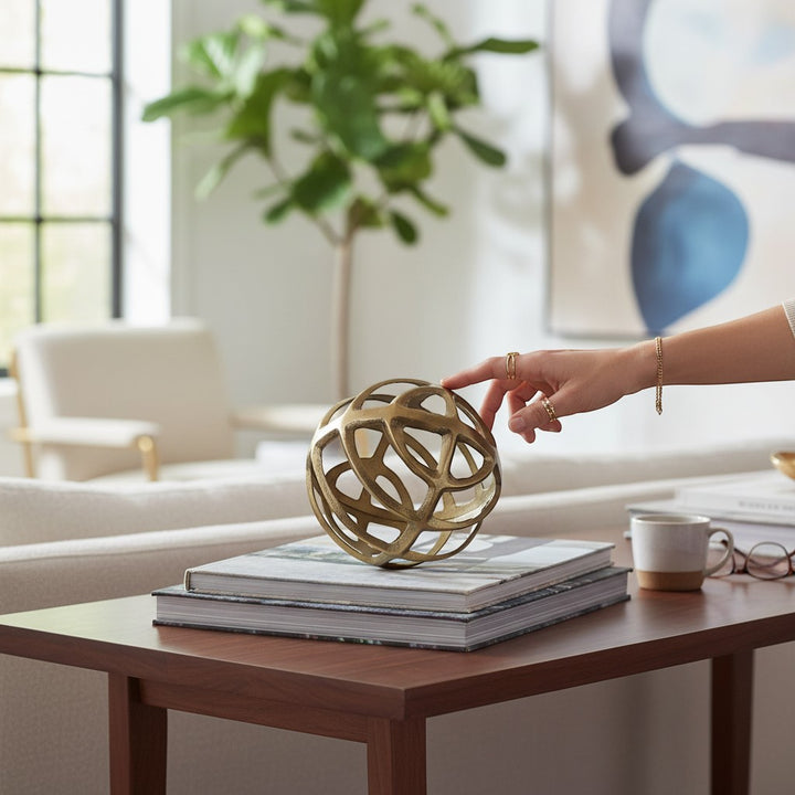 Chic Collective gold metal geometric sphere decor on stacked books, featuring an open, intersecting rod design.