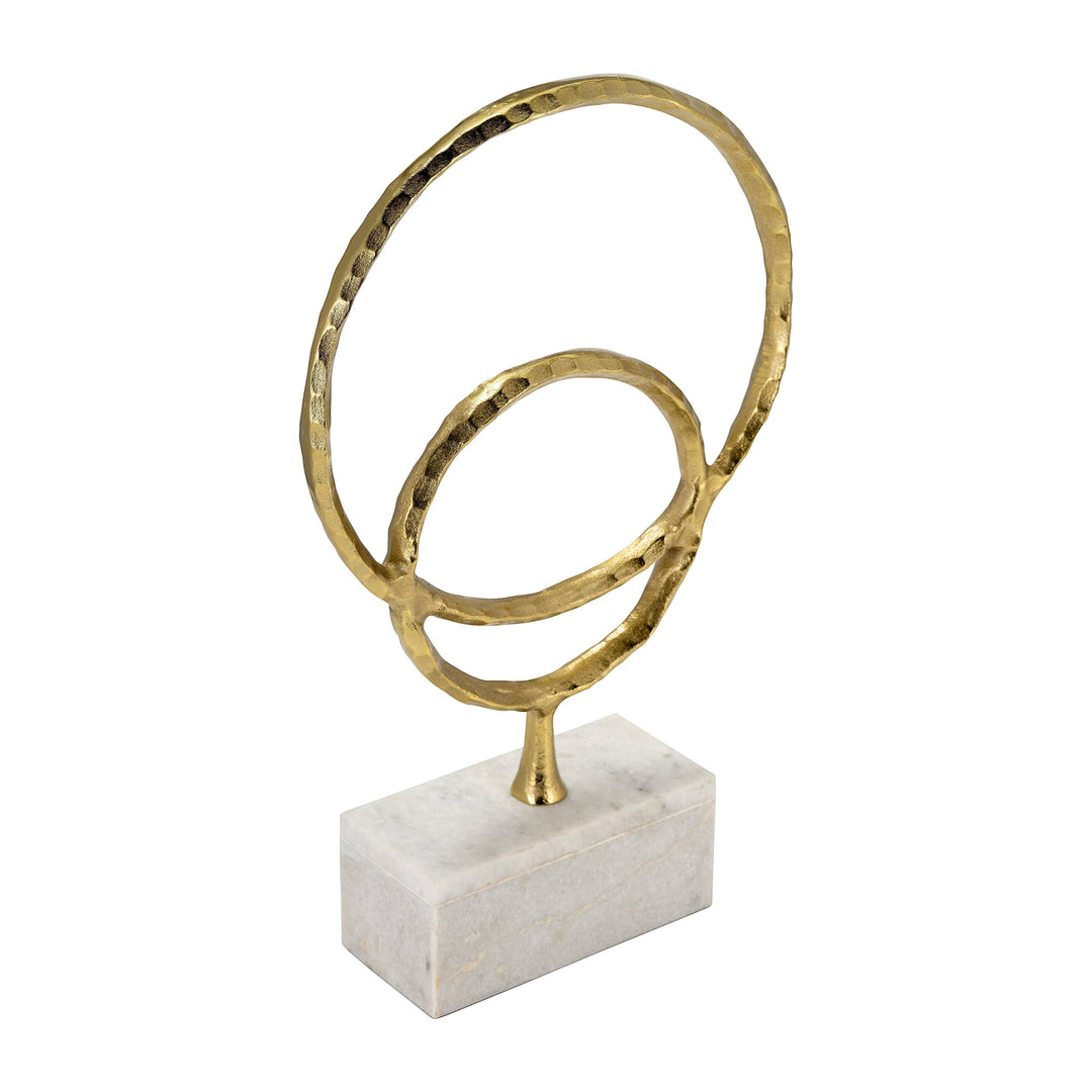Chic Collective gold metal abstract double ring sculpture with hammered texture on a white marble rectangular base.