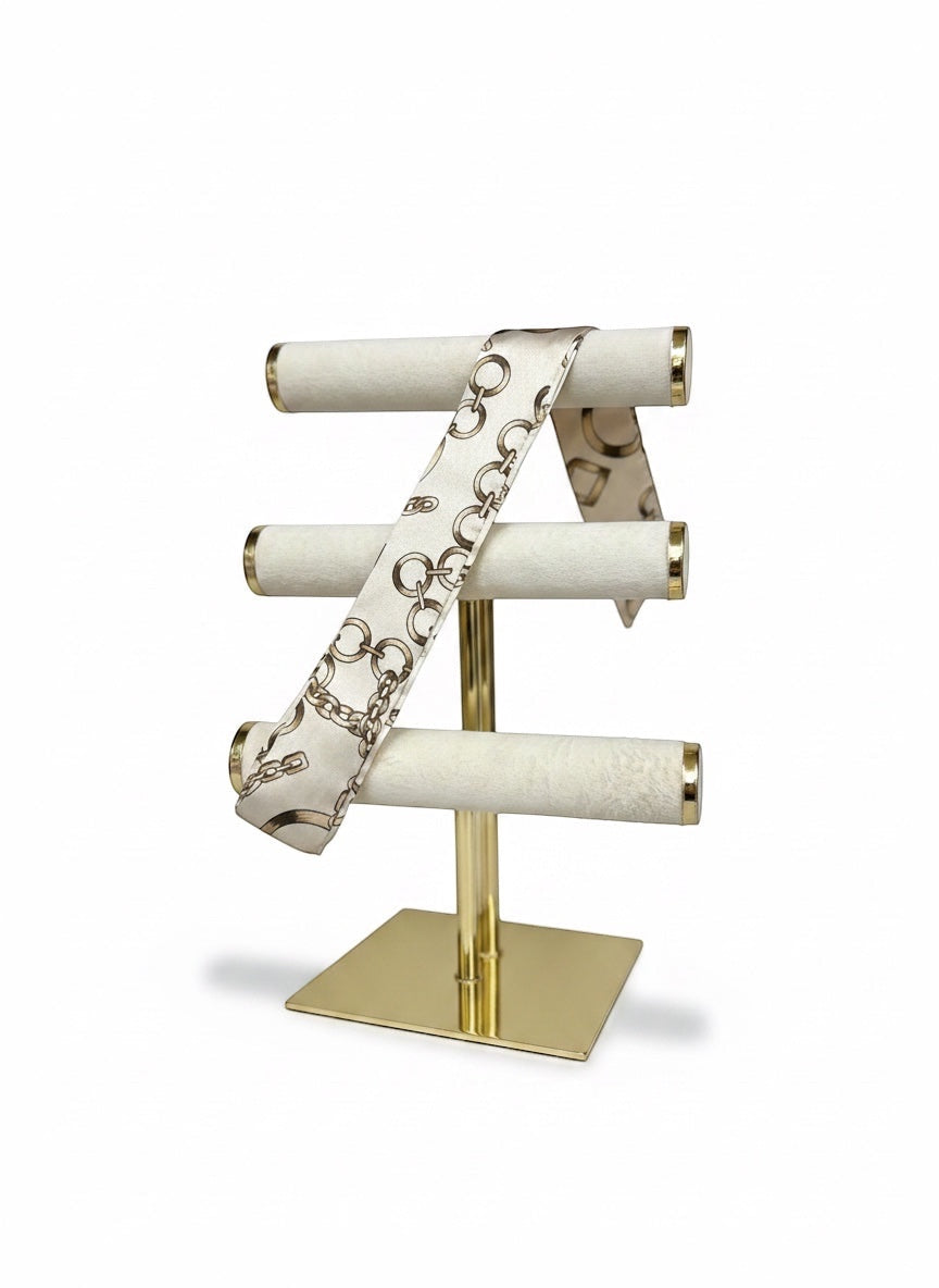 Chic Collective Golden Link Ribbon Tie, a satin scarf with a gold chain print on an ivory background, displayed on a gold stand.