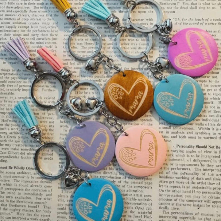Chic Collective Mama keychain with a heart design and tassel in pastel colors: pink, purple, blue, and wood.