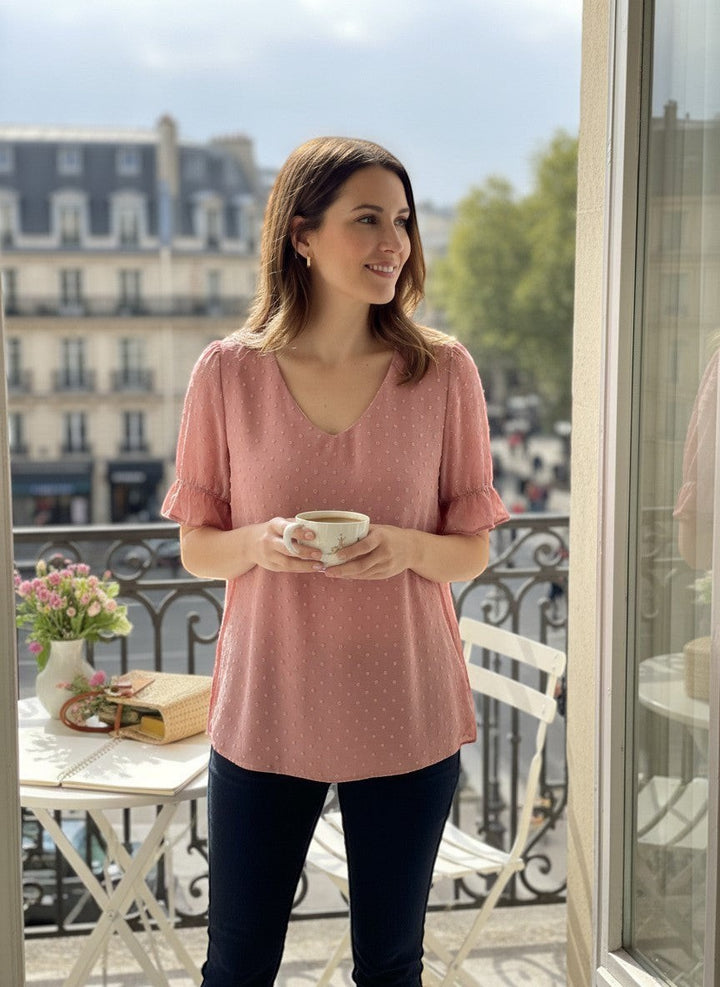 Chic Collective mauve Swiss dot v-neck top with ruffled short sleeves, worn by a woman holding a coffee cup on a balcony.