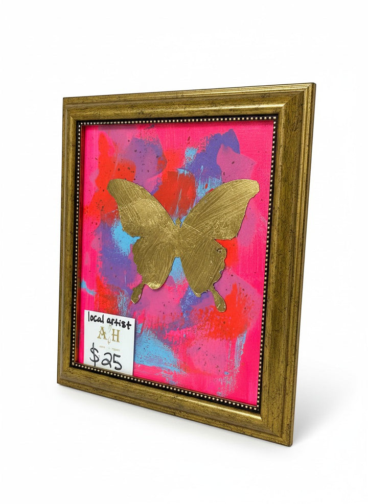 Chic Collective Neon Flutter framed artwork featuring a gold metallic butterfly on a vibrant abstract background of hot pink, coral, violet, and blue.