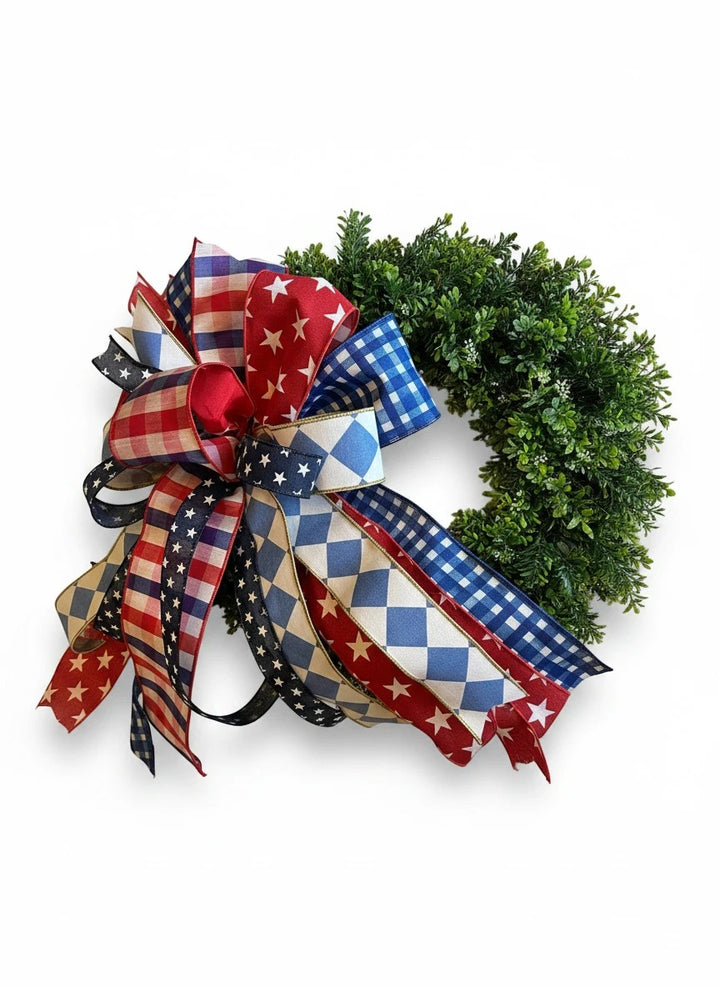 Chic Collective patriotic bow with red, white, and blue stars, plaid, gingham, and diamond patterns on a greenery wreath.