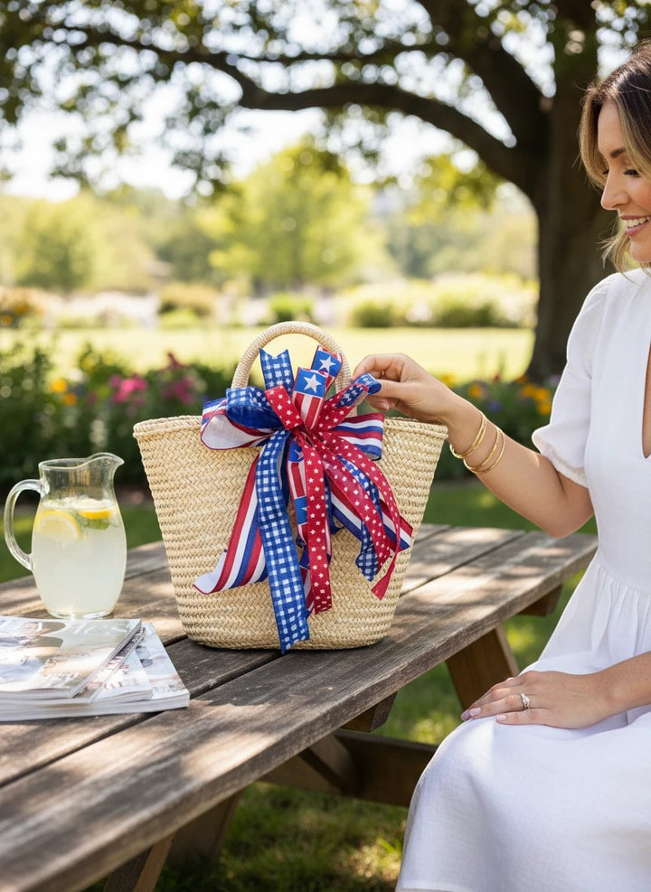 Chic Collective patriotic ribbon bow with red, white, and blue stars and stripes on a straw tote bag outdoors
