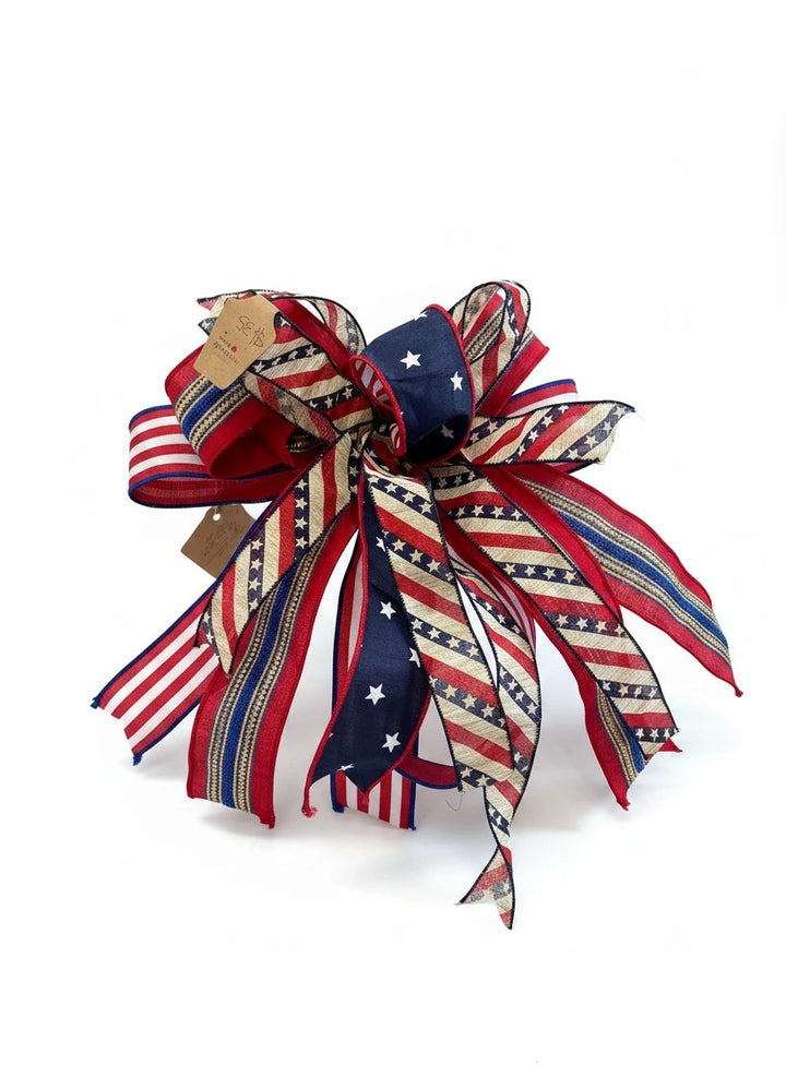 Chic Collective patriotic ribbon bow featuring red, white, and blue stars and stripes on rustic textured fabric.