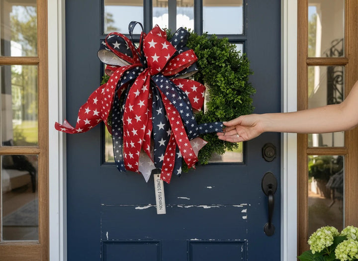 Chic Collective patriotic wreath with red, white, and blue star ribbon bow on a green base, hanging on a navy door.