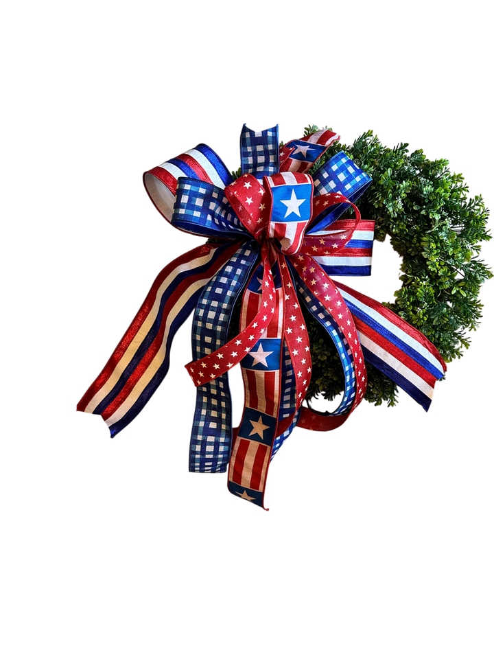 Chic Collective patriotic bow with red, white, and blue ribbons featuring stars and gingham patterns, attached to a green wreath.