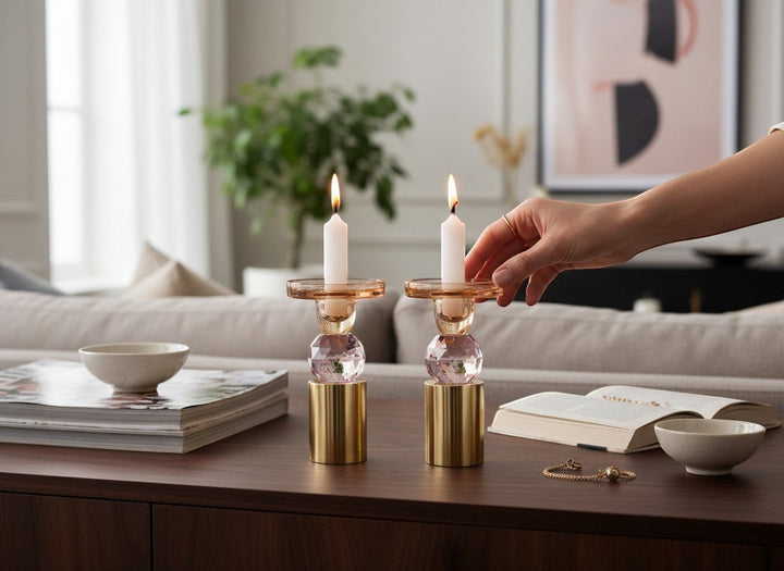 Chic Collective set of 2 pink and amber crystal candlesticks, 6.5"H, with gold bases, on a wooden table.