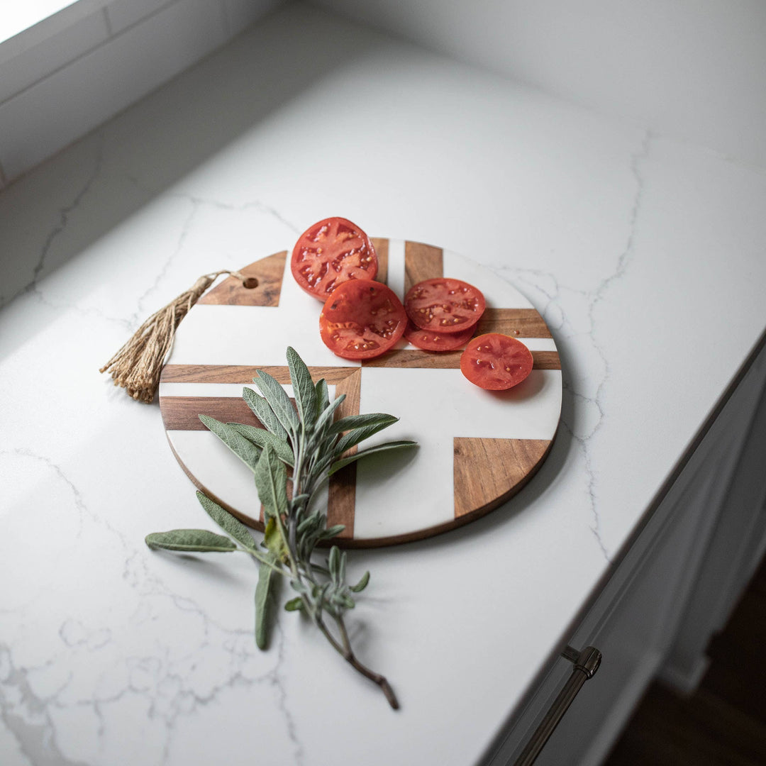 Chic Collective Clement round cutting board with white resin and wood inlay, featuring sliced tomatoes and sage.