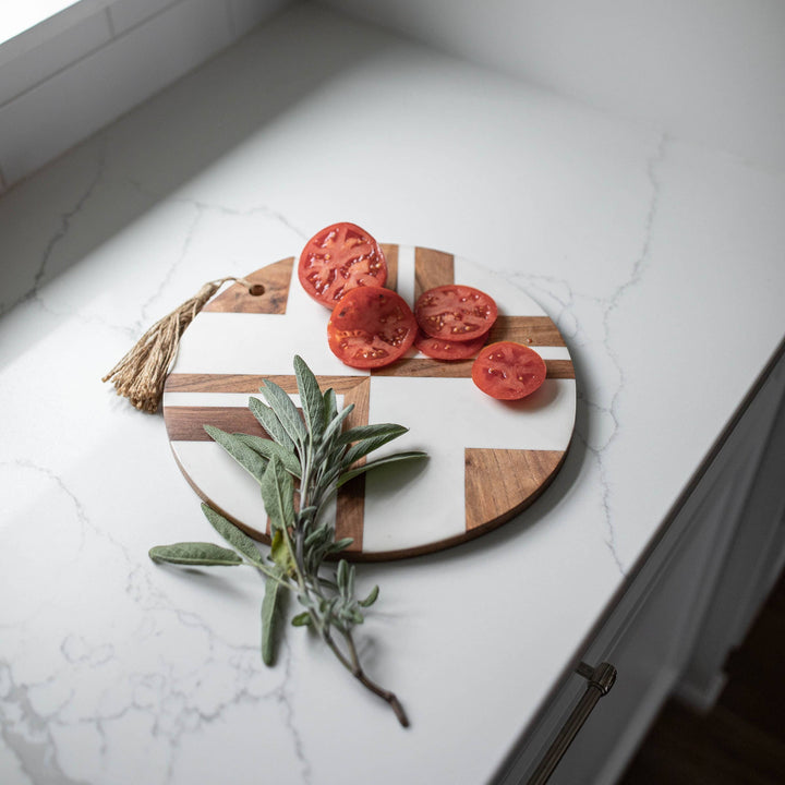 Chic Collective Clement round cutting board with white resin and wood inlay, featuring sliced tomatoes and sage.