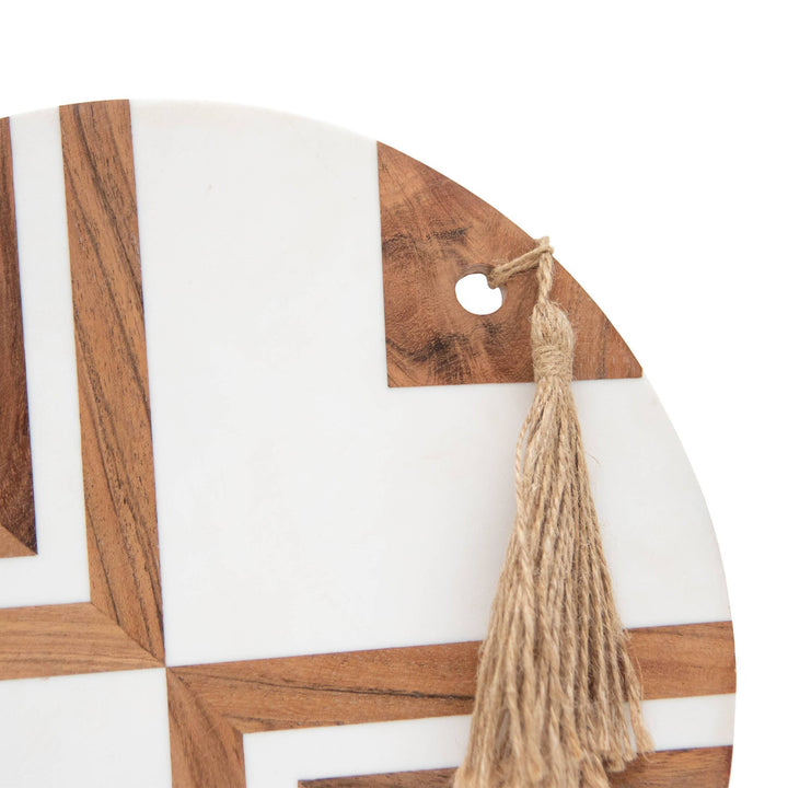 Chic Collective Clement large round cutting board with white resin inlay and acacia wood geometric pattern, featuring a jute tassel.