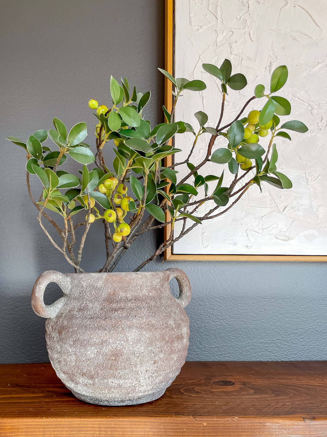 Chic Collective Siena rustic vintage-style ceramic vase with handles, featuring earthy tones and a textured finish. Holds green foliage with yellow berries.