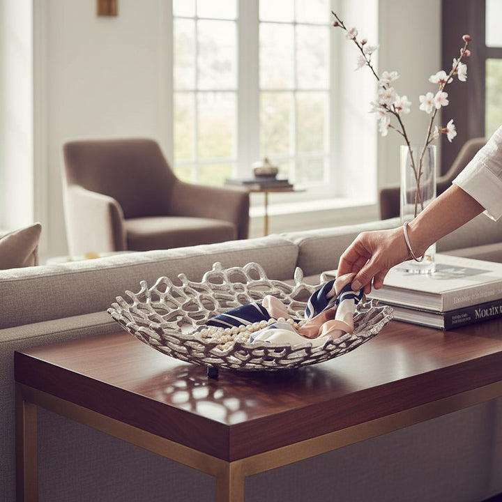 Chic Collective 15-inch silver aluminum coral decorative bowl with a rough-hewn, openwork design, holding scarves and pearls.