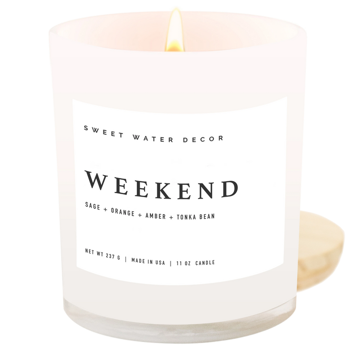 Chic Collective Weekend 11 oz soy candle in a white jar with a lit wick. Scent notes include citrus, grapefruit, sage, lavender, amber, tonka bean, and oakmoss.