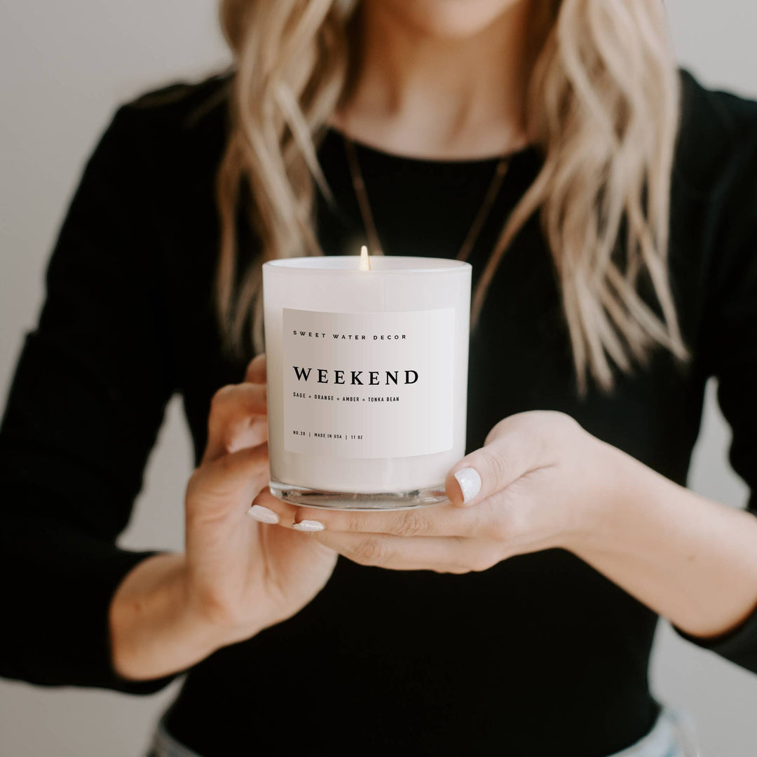 Chic Collective Weekend 11 oz soy candle in a white jar with a lit wick. Scent notes: Citrus, Grapefruit, Sage, Lavender, Amber, Tonka Bean, Oakmoss.