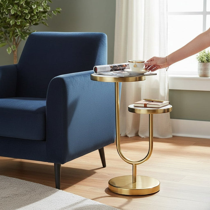 Chic Collective two-tier round end table with white marble tops and gold iron base, next to a blue armchair.