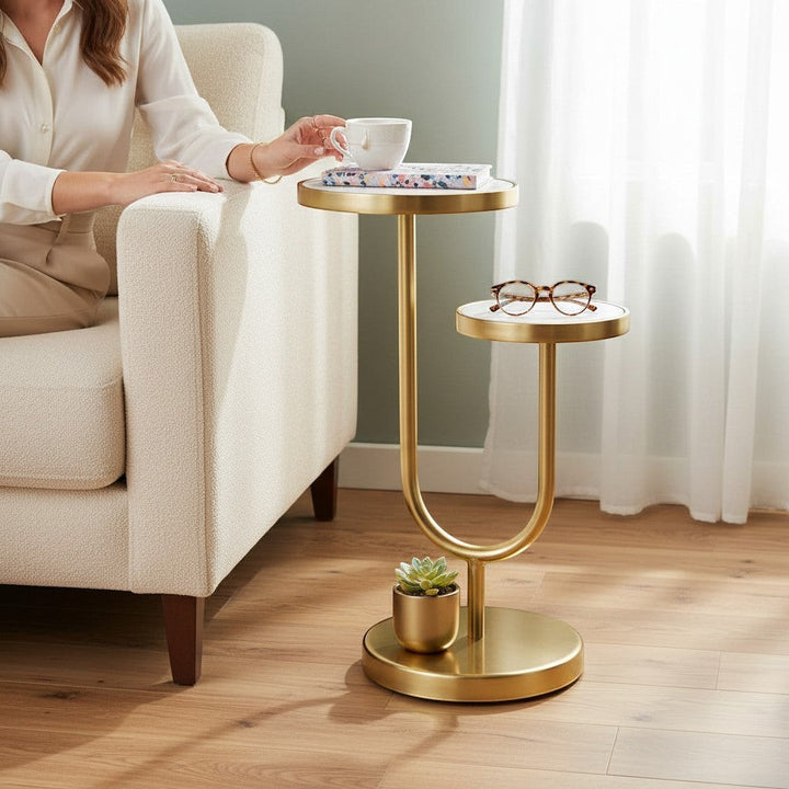 Chic Collective 22" white marble and gold iron two-tier round end table with a U-shaped base, next to a cream sofa.