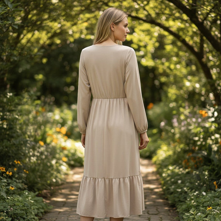 Chic Collective beige long-sleeve ruched maxi dress with tiered hem, worn by a blonde model in a garden setting.