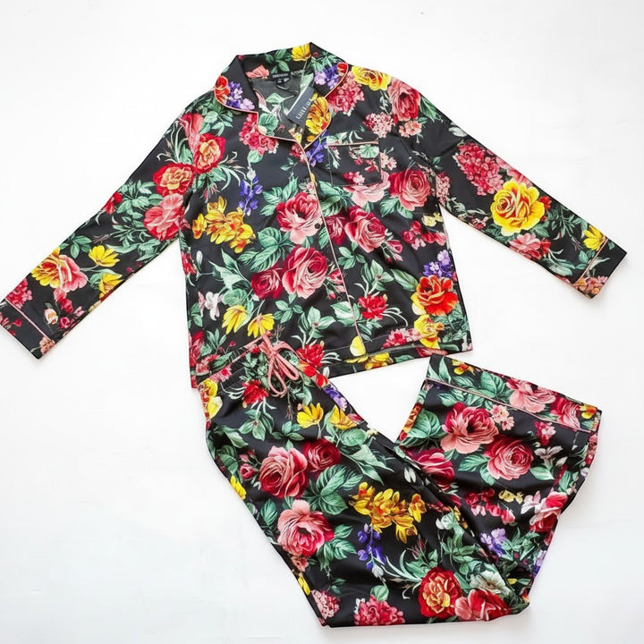 Chic Collective black satin pajama set with a vibrant floral print. Features a collared long-sleeve top and matching wide-leg pants.