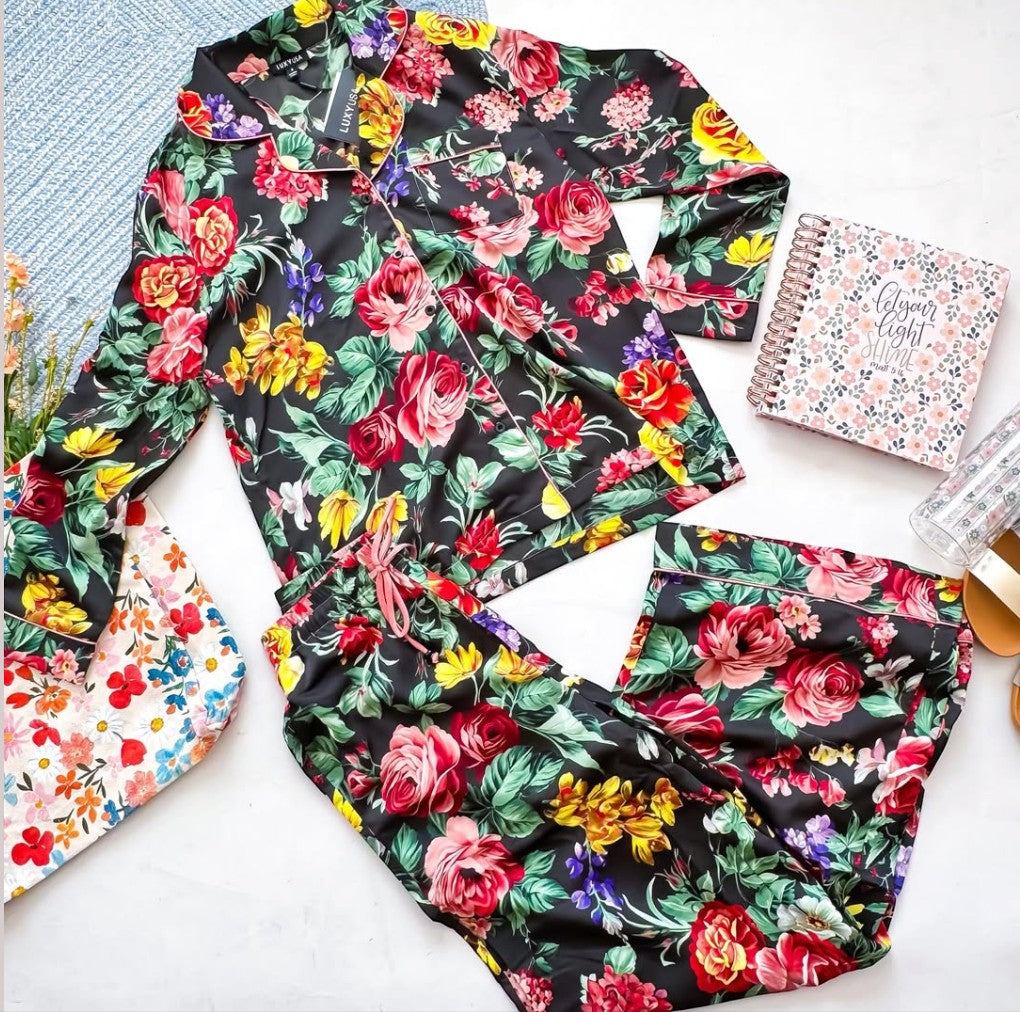 Chic Collective black satin pajama set with a vibrant floral print of red roses, yellow flowers, and purple accents. Features a collared button-up top and drawstring pants.