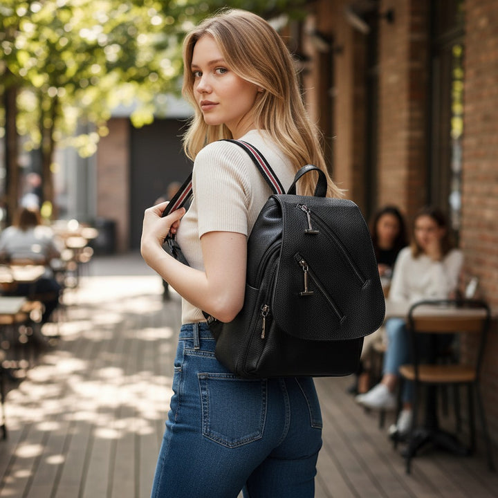Chic Collective black textured leather backpack with diagonal zipper details and striped adjustable shoulder straps, worn by a woman.