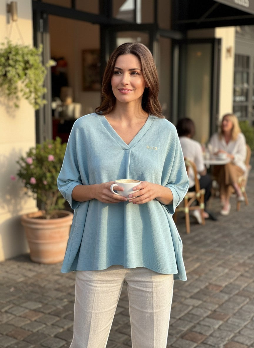 Chic Collective light blue textured V-neck dolman sleeve top with a relaxed fit, paired with light beige trousers.