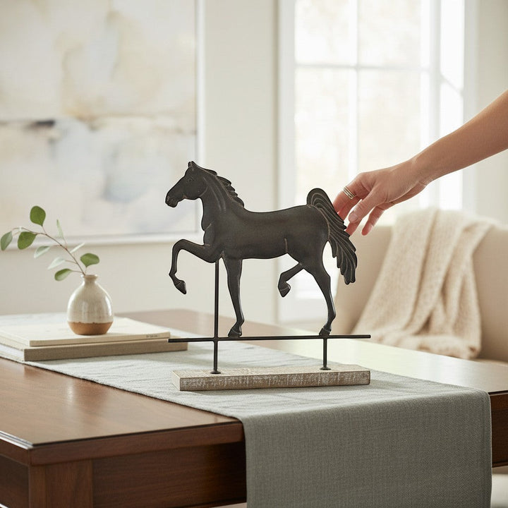 Chic Collective dark metal horse sculpture on a rustic wood base with a stand, displayed on a table runner.