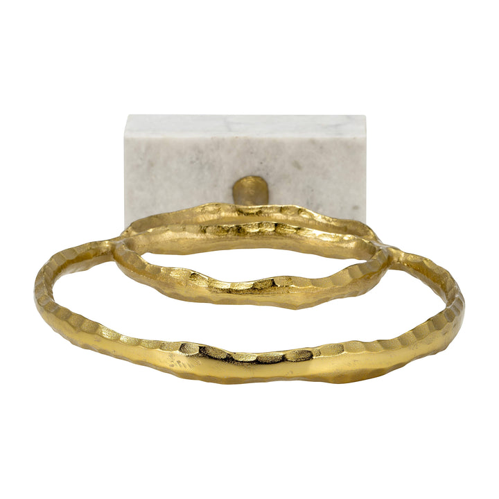 Chic Collective gold metal double ring sculpture with hammered texture on a white marble base.
