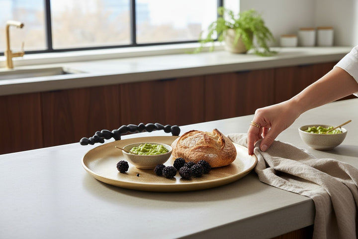 Chic Collective gold round serving tray with black pebble handles, holding bread, dip, and berries.