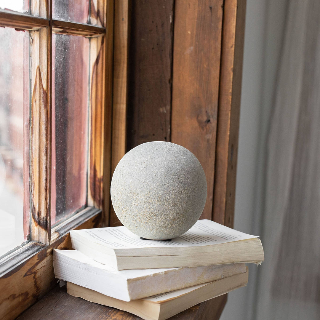 Chic Collective coastal gray textured terracotta deco ball with sandy, stone-like finish, displayed on stacked books.