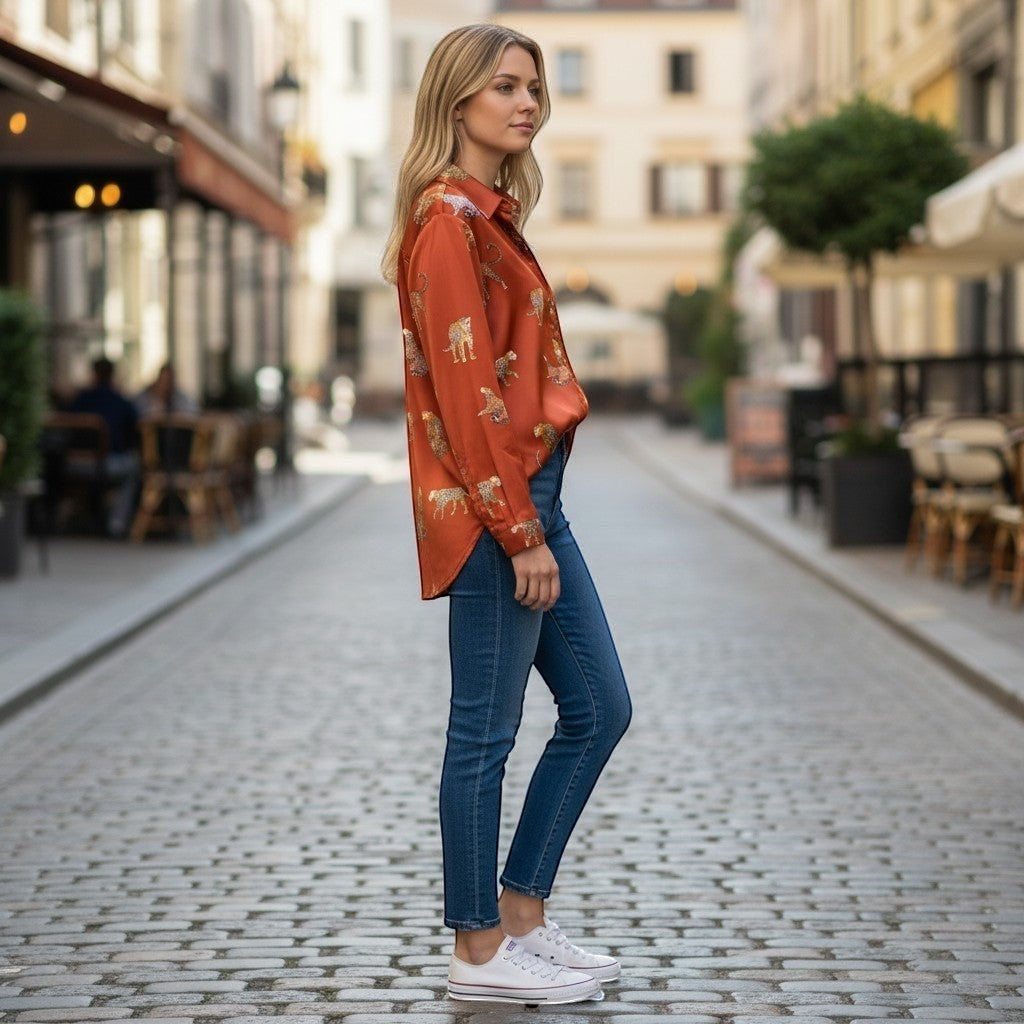 Chic Collective rust orange long-sleeve button-up shirt with a repeated leopard print pattern, worn by a woman with blonde hair standing on a cobblestone street.