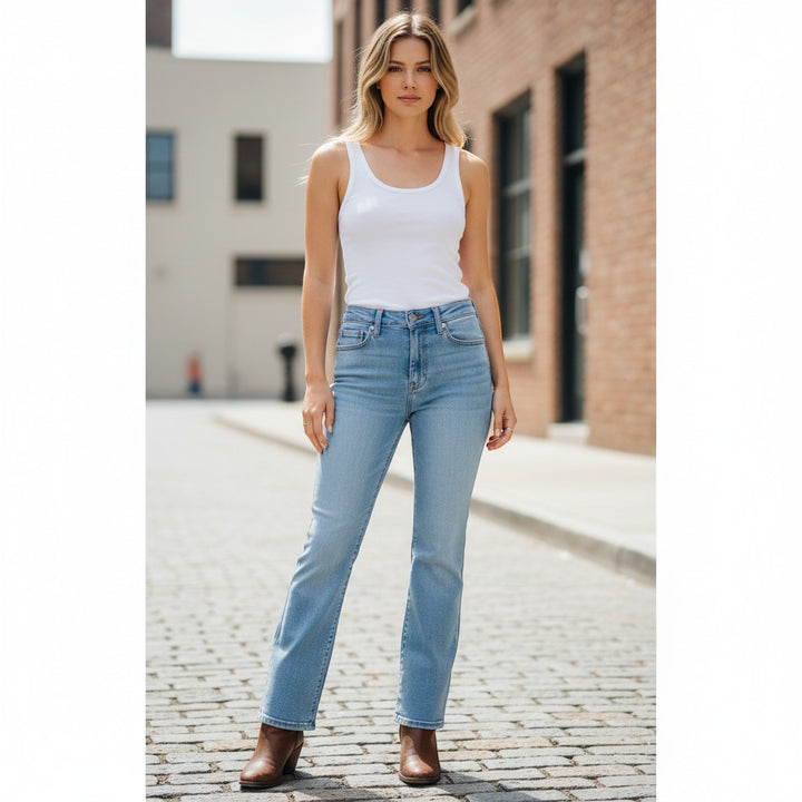 Chic Collective Risen Mid Rise light wash denim jeans with frayed hem, worn by a model standing on a cobblestone street.