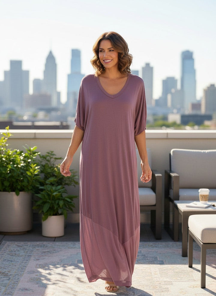 Chic Collective mauve dolman sleeve maxi dress with V-neck and flowing silhouette, worn by a model on a rooftop with city skyline.