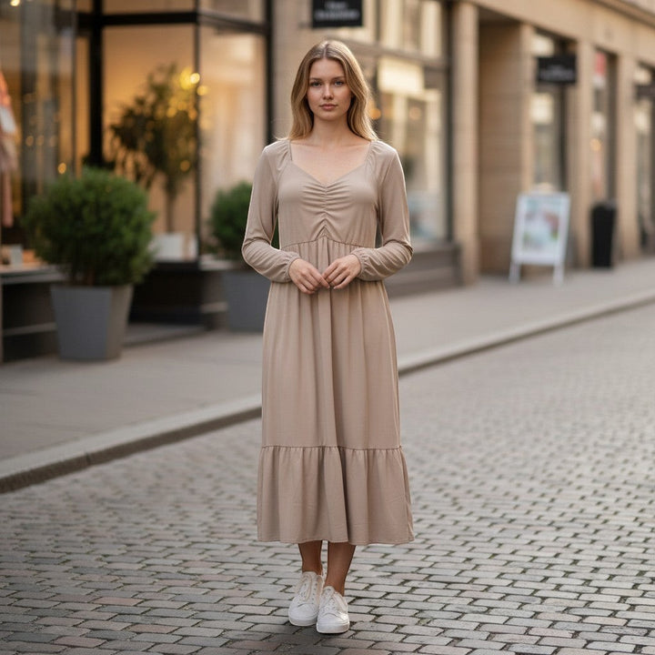 Chic Collective mauve ruched maxi dress with long sleeves and tiered hem, worn by a woman on a cobblestone street.