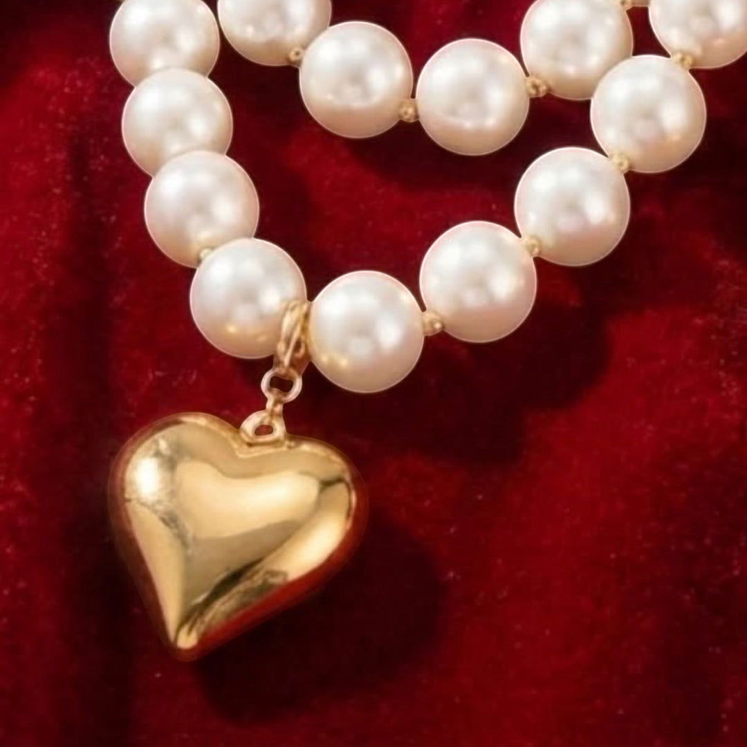 Chic Collective pearl necklace with a gold-tone heart charm on a red velvet background.