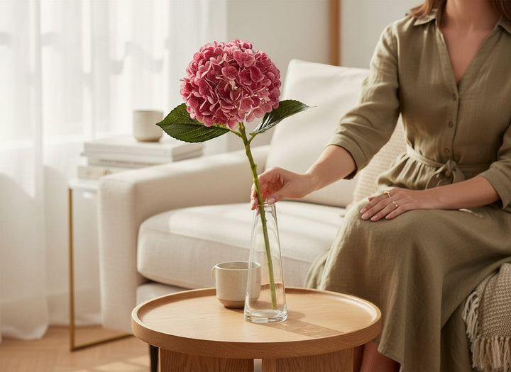 Chic Collective Real Touch Hydrangea stem in pink with green leaves, 18.5" long, in a glass vase.