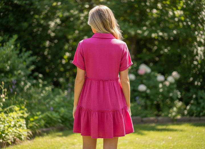 Chic Collective pink mineral wash tiered mini dress with short sleeves and collar, shown on a woman from behind in a garden setting.