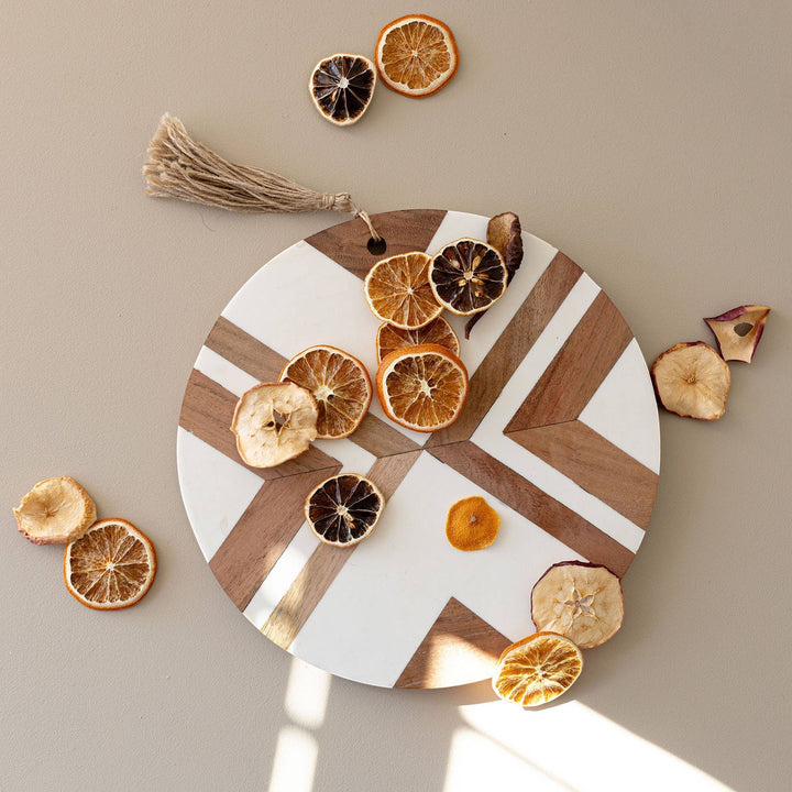 Chic Collective Clement large round cutting board with white resin inlay and acacia wood geometric pattern, featuring dried fruit.