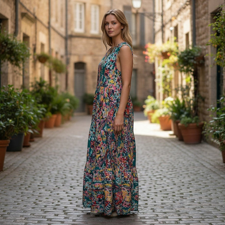 Chic Collective teal tiered sleeveless maxi dress with a vibrant floral print and flowing silhouette, worn by a model on a cobblestone street.