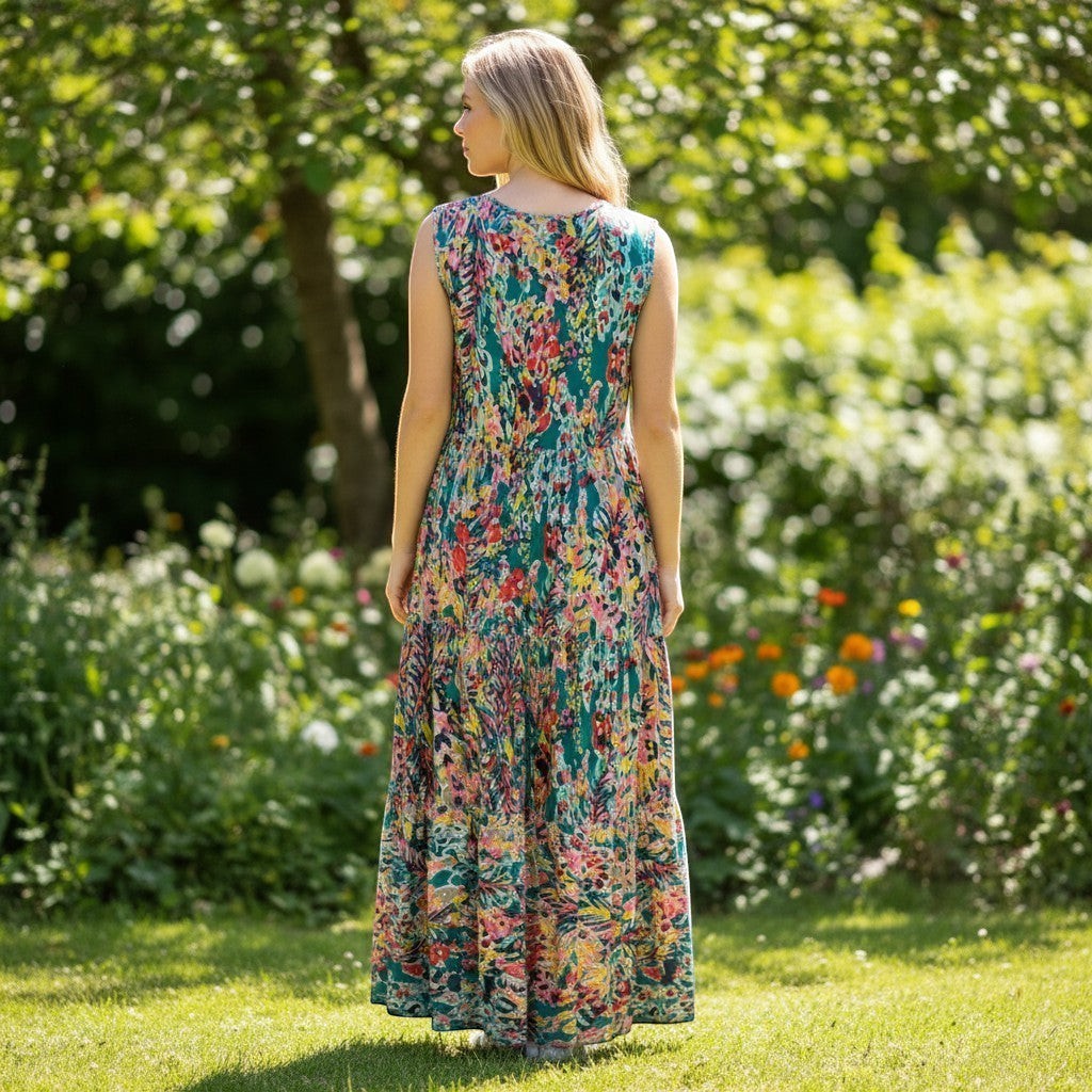 Chic Collective teal tiered sleeveless maxi dress with a vibrant floral print and flowing silhouette, worn by a woman in a garden.
