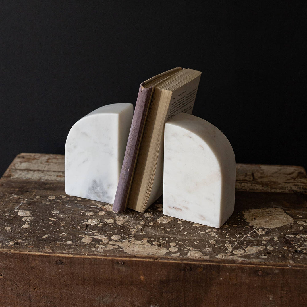 Chic Collective white marble arch bookends with a book between them, adding a modern sculptural accent to a shelf.