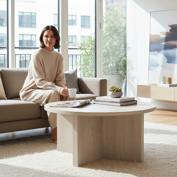 Chic Collective modern white round coffee table made of manufactured wood with a minimalist design, shown in a living room setting.