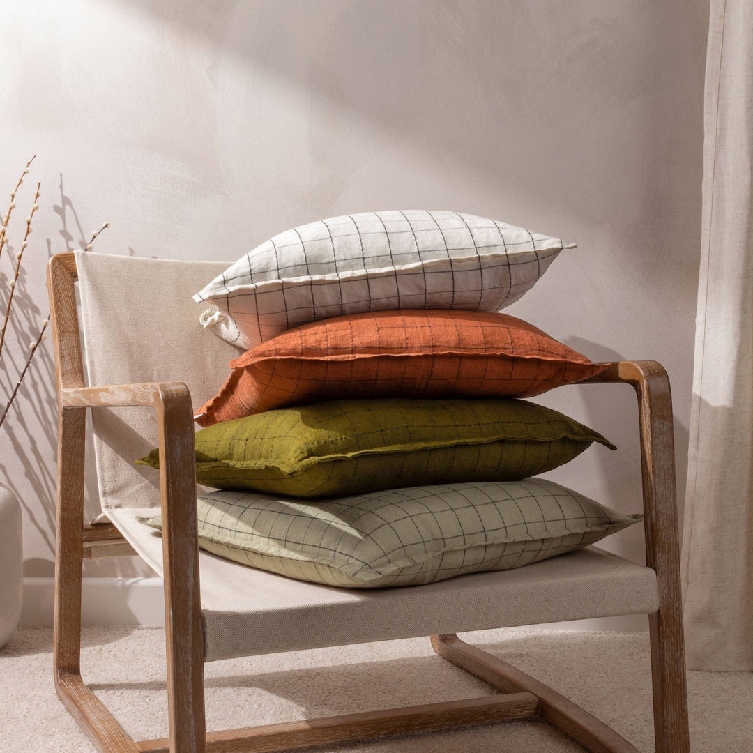 Chic Collective ecru linen grid check cushion with flange twin-stitched edge, stacked on a chair with other coloured cushions.