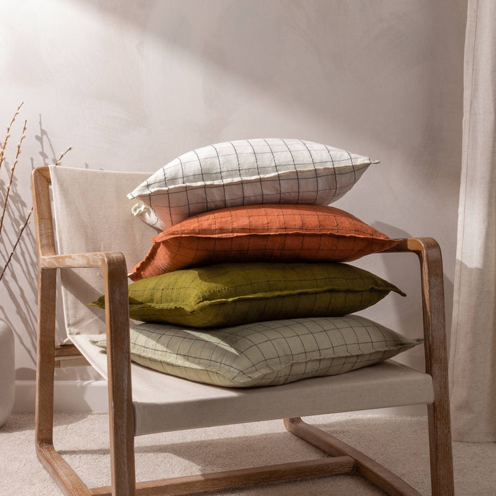 Chic Collective ecru linen grid check cushion with flange twin-stitched edge, stacked on a chair with other coloured cushions.